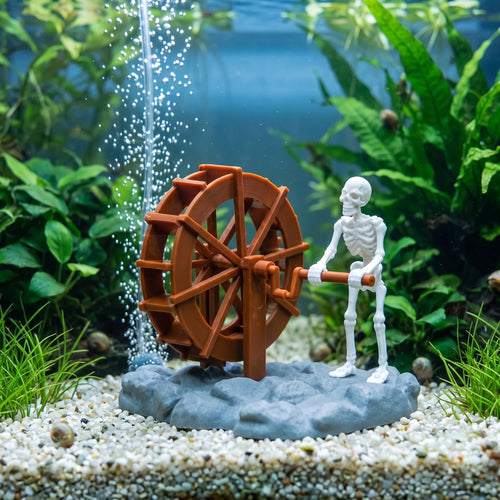Skeleton and waterwheel ornament standing on gravel in a planted aquarium
