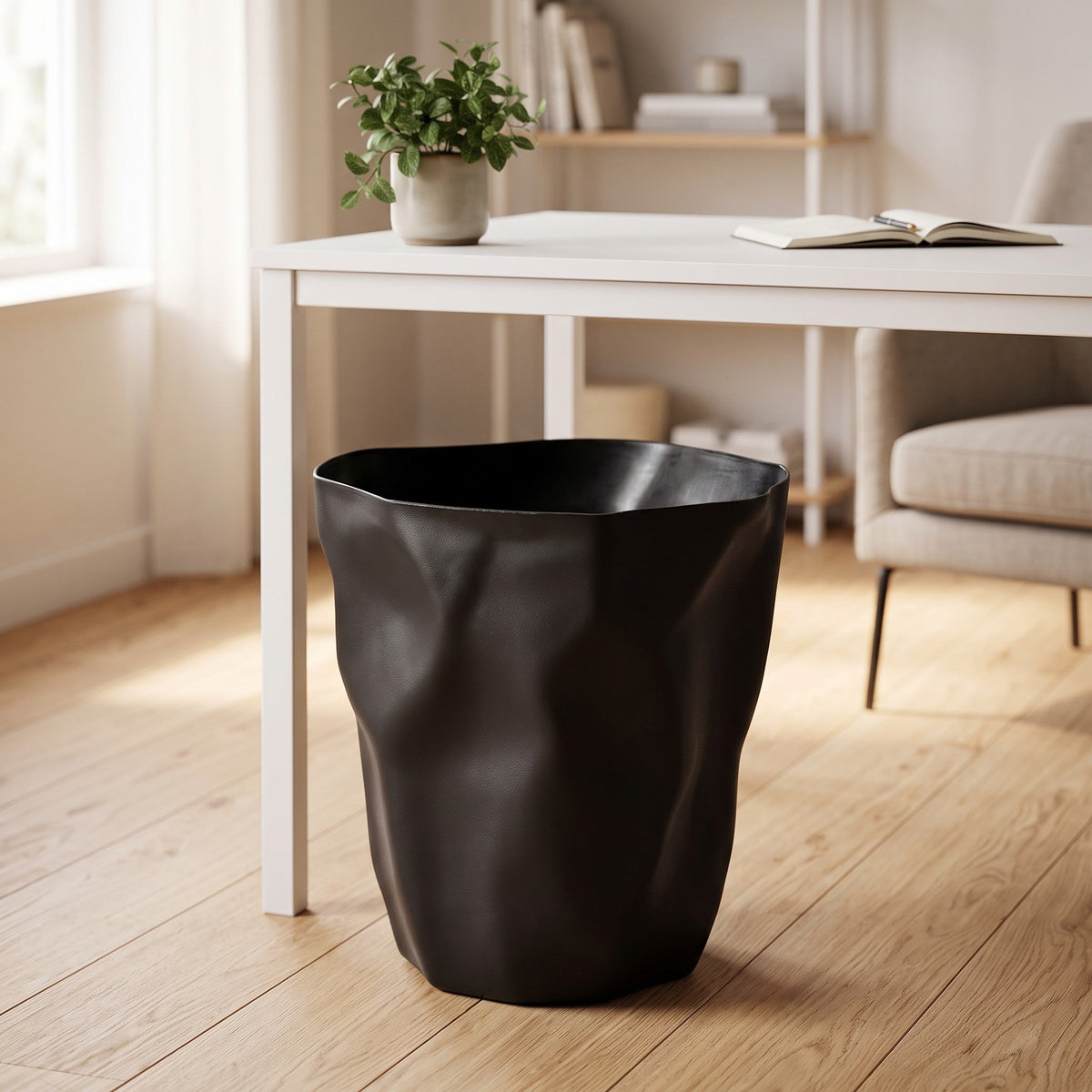 Black crumpled-shape trash can beside a white desk in a home office