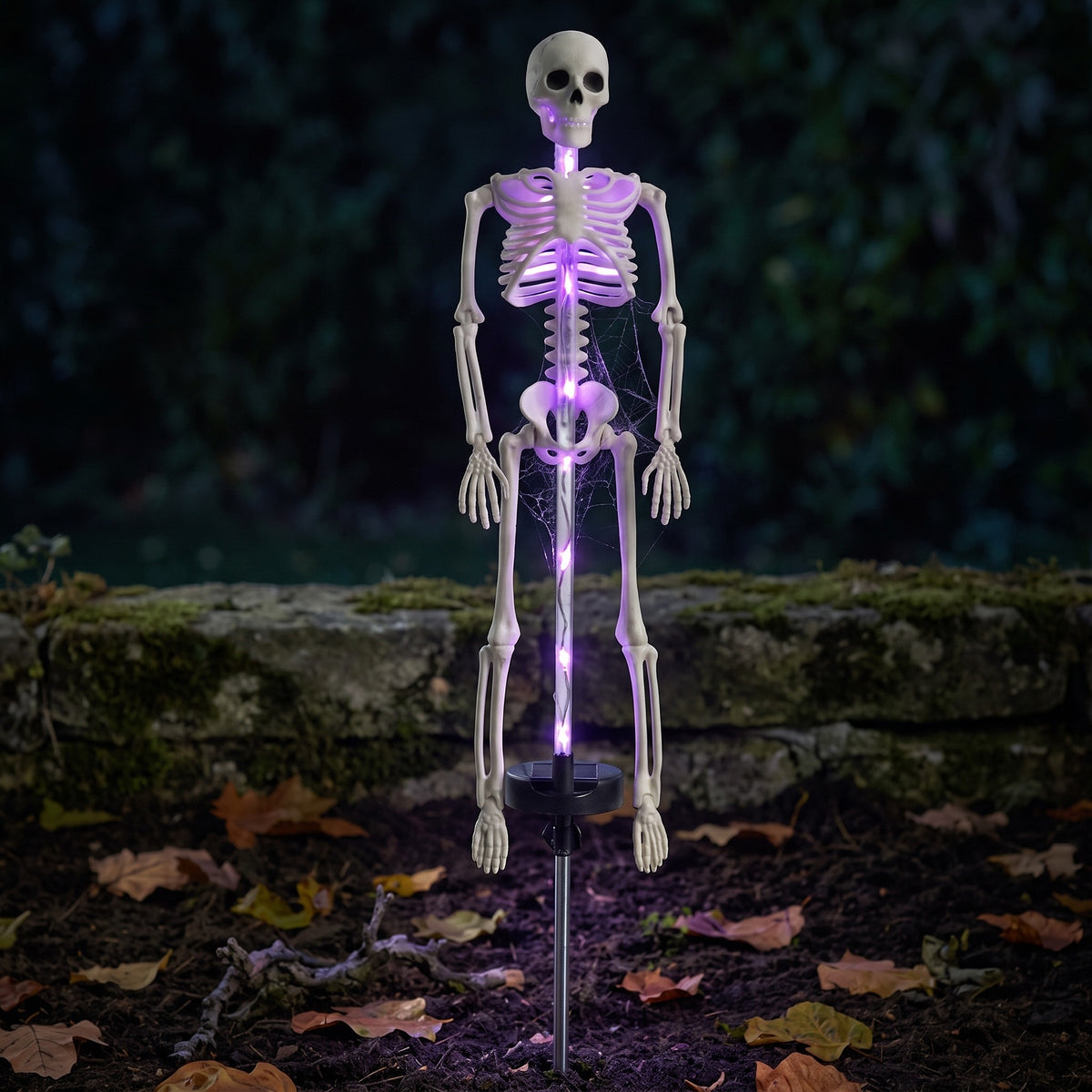 Solar skeleton stake light glowing in a garden bed at night